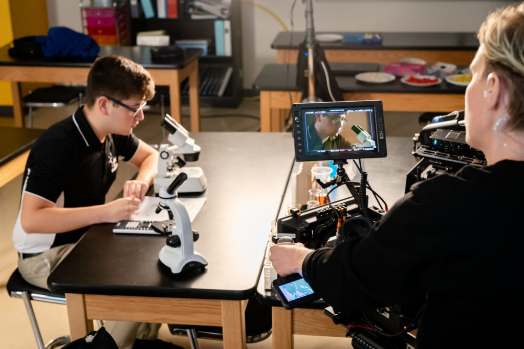 Crew filming student looking at microscope